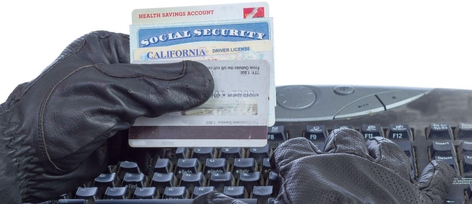 Close-up of a hand holding multiple ID cards and typing info, symbolizing identity theft and data breach risk.